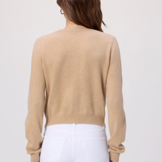 Woman wearing a beige sweater and white pants on a plain background