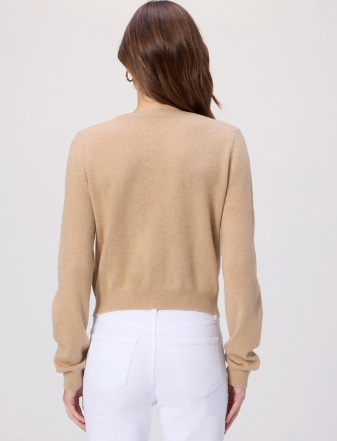 Woman wearing a beige sweater and white pants on a plain background