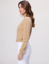 Woman wearing a beige sweater and white pants on a plain background