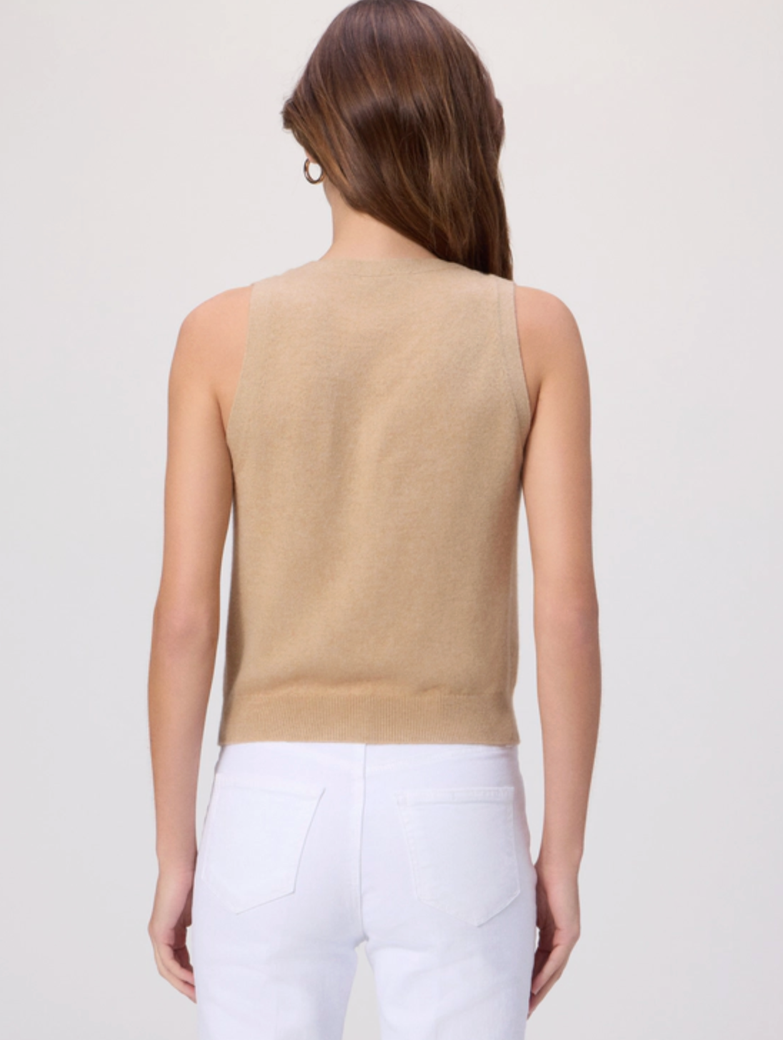 Woman wearing a beige sleeveless top and white pants on a light gray background