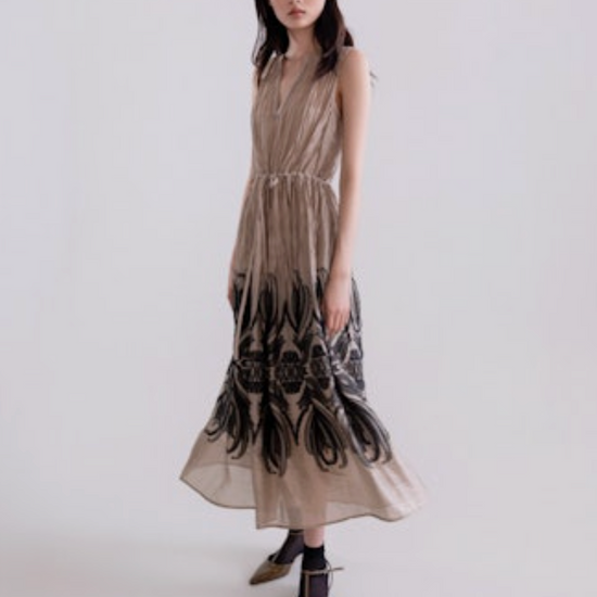 Woman wearing a long, patterned dress against a plain background