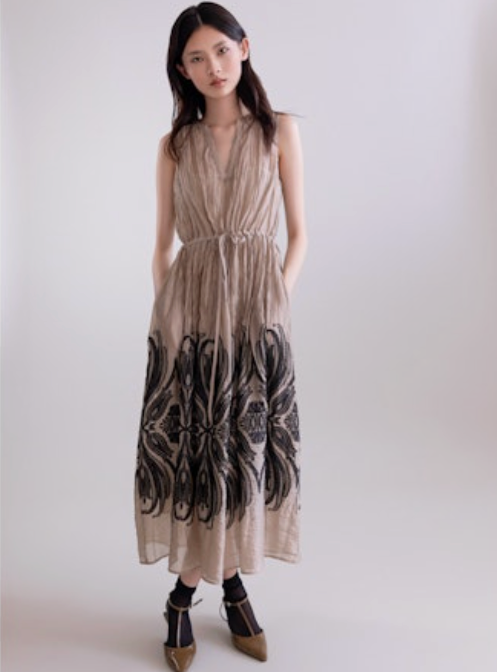 Woman wearing a sleeveless dress with a pattern on a plain background