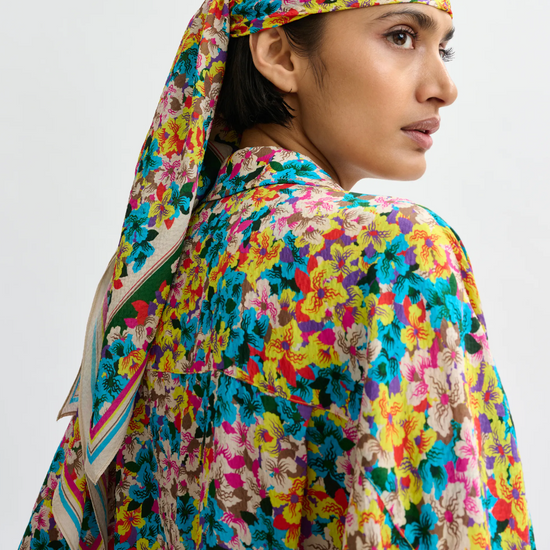 Person wearing a colorful floral headscarf and outfit on a plain background