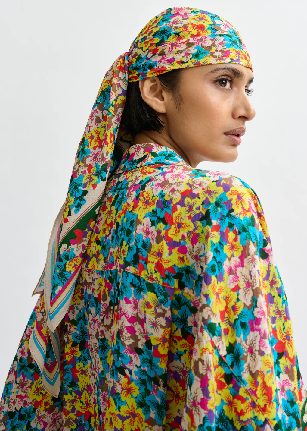 Person wearing a colorful floral headscarf and outfit on a plain background