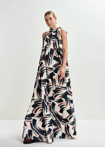 Woman wearing a sleeveless, long, patterned dress on a white background