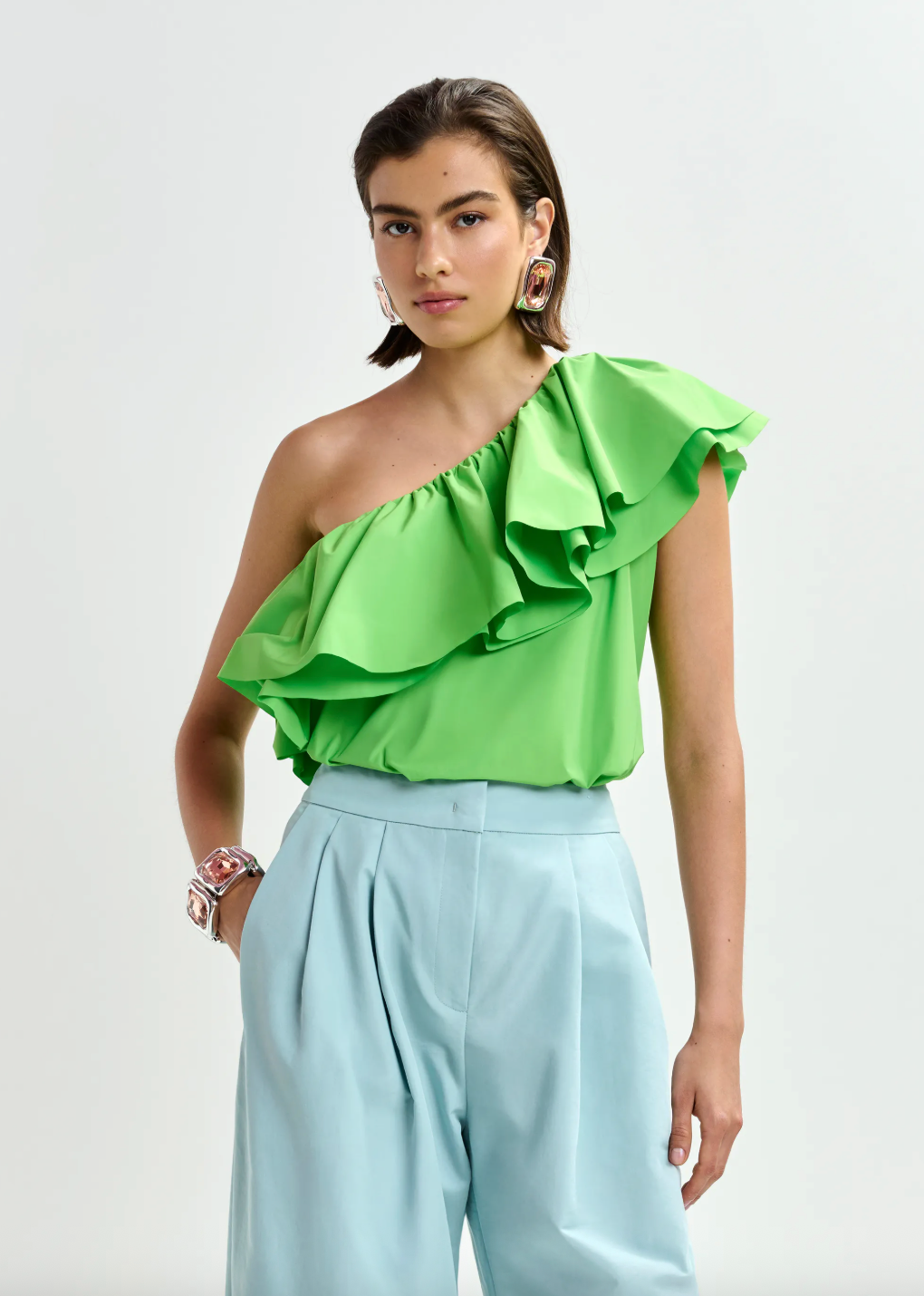Bright green one shoulder top worn with pale blue trousers