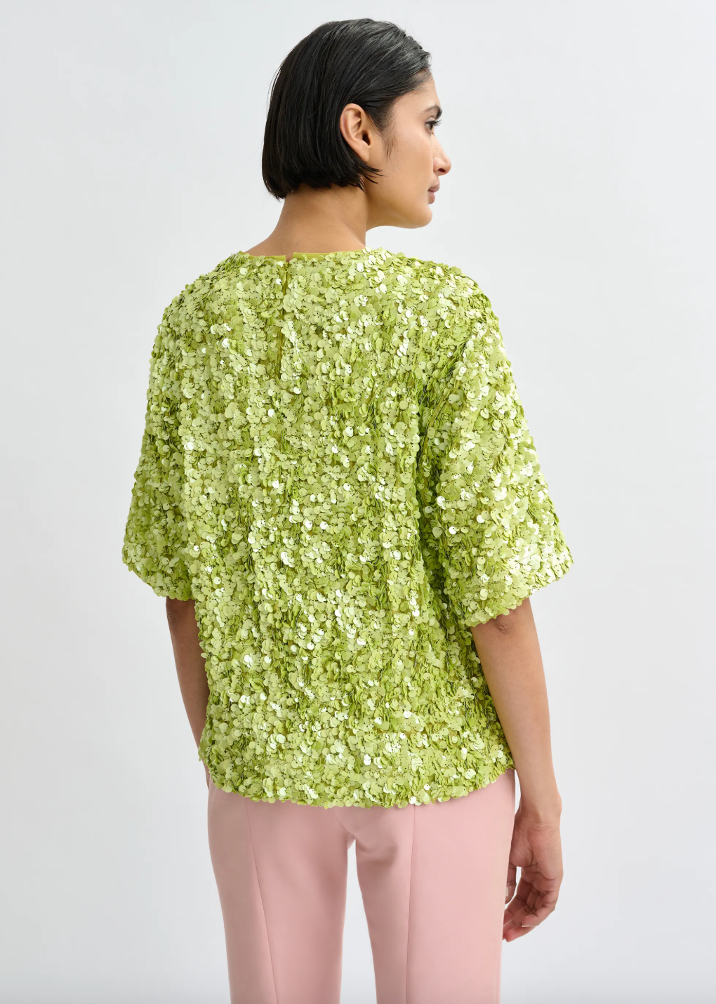 Woman wearing a green floral blouse and pink pants on a white background