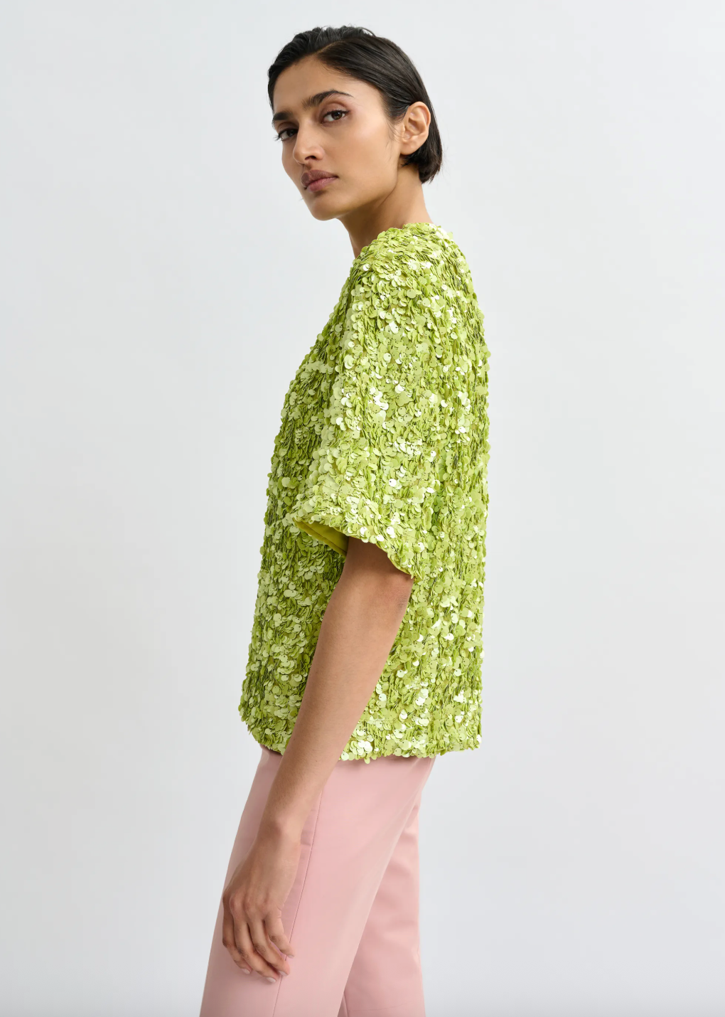 Woman wearing a green floral top and pink pants on a white background