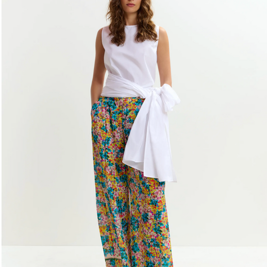 Woman wearing a white sleeveless top and colorful floral pants on a white background