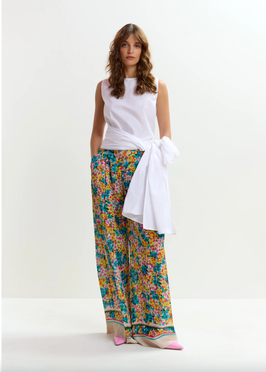 Woman wearing a white sleeveless top and colorful floral pants on a white background