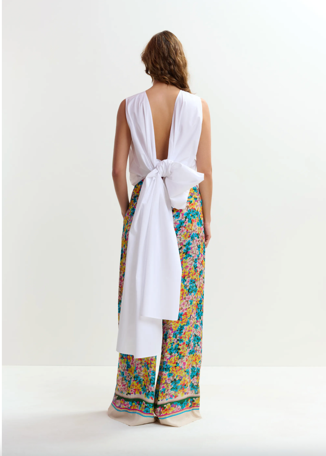 Woman wearing a white top and colorful floral pants on a white background