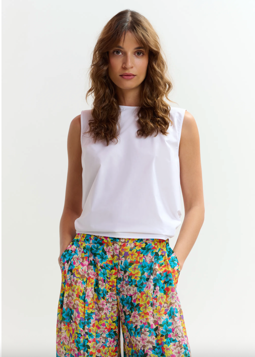 Woman wearing a white sleeveless top and colorful floral pants on a white background