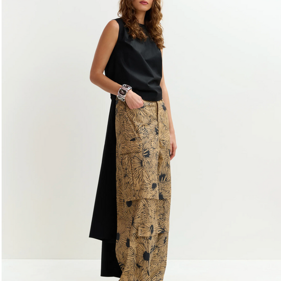 Woman wearing a black sleeveless top and patterned beige pants on a white background