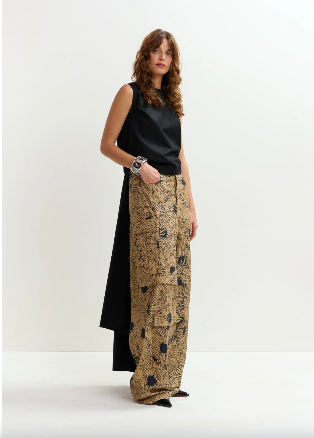 Woman wearing a black sleeveless top and patterned beige pants on a white background