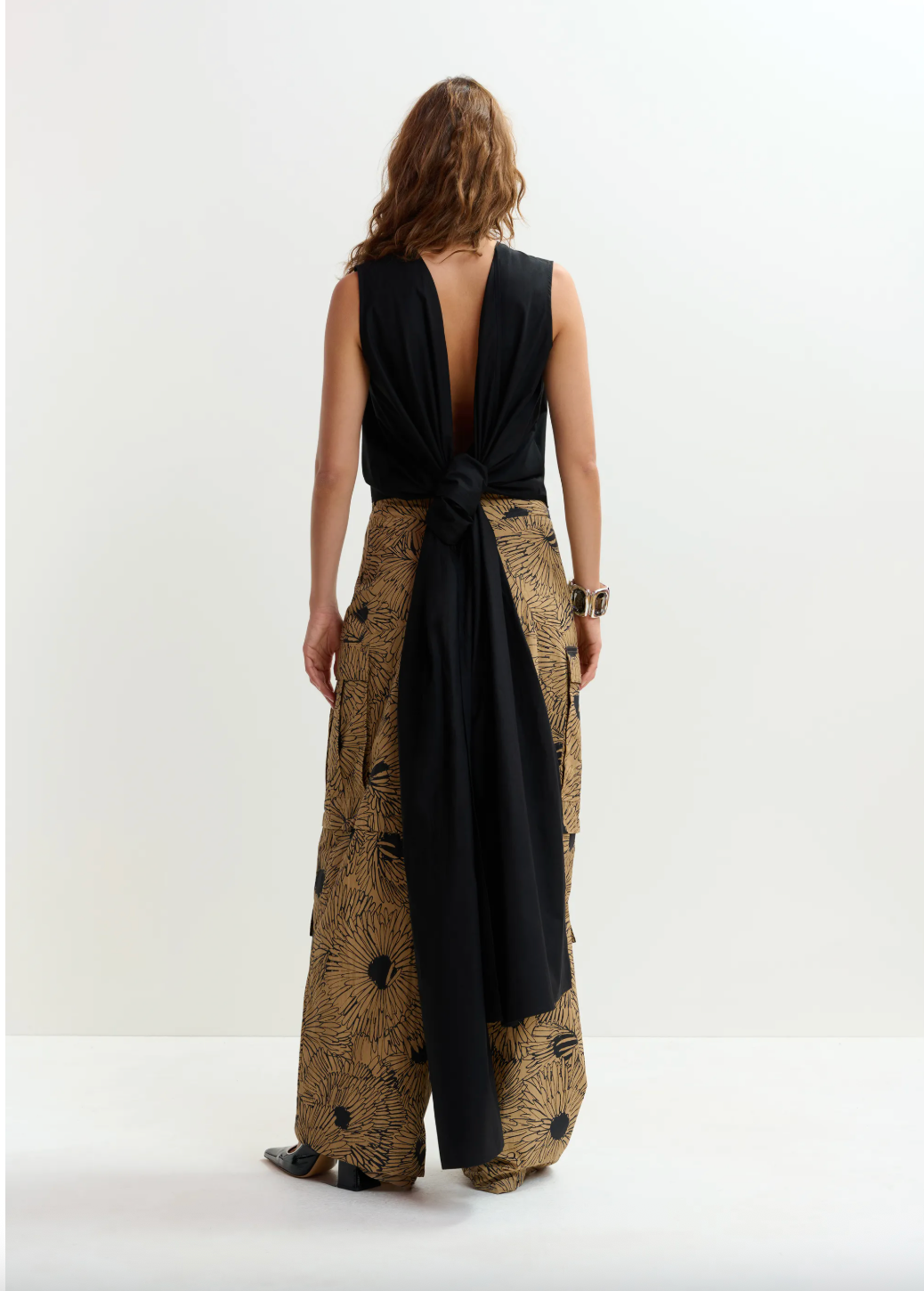 Woman wearing a black sleeveless top and patterned wide-leg pants on a white background