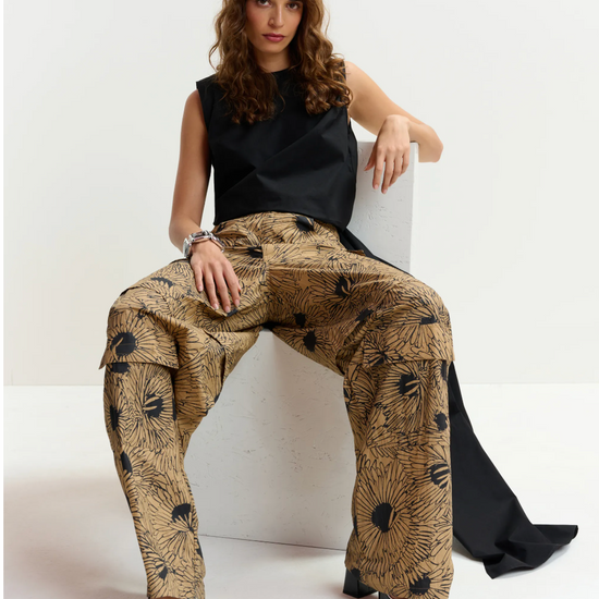 Woman sitting on a chair wearing a black top and patterned beige pants.