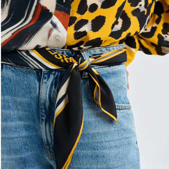 Close-up of a person wearing a patterned top with a scarf tied around their waist, on a white background.