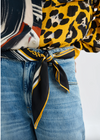 Close-up of a person wearing a patterned top with a scarf tied around their waist, on a white background.