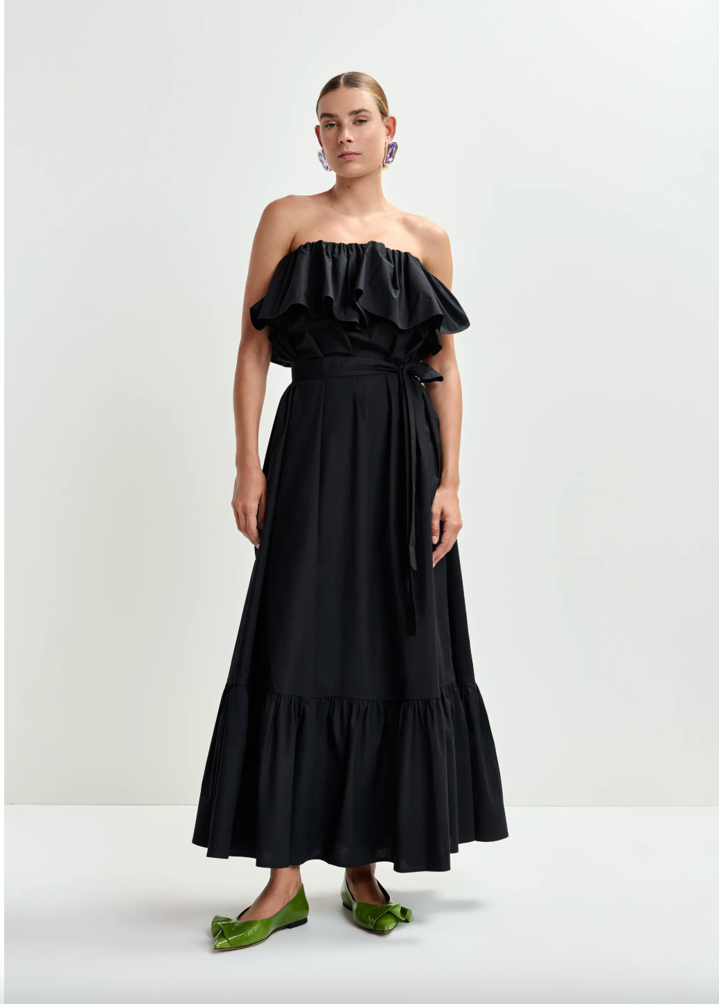 Woman wearing a black off-shoulder dress with ruffled top on a white background