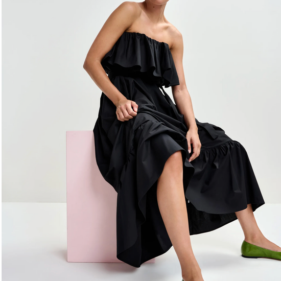Woman in a black strapless dress sitting on a pink stool against a white background