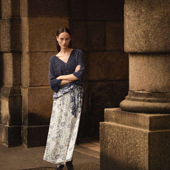 Woman in a blue top and patterned skirt standing in a stone archway