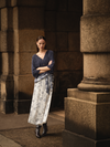 Woman in a blue top and patterned skirt standing in a stone archway