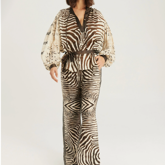 A model wearing a matching zebra-print jumpsuit with a brown belt, photographed against a plain light gray studio background.