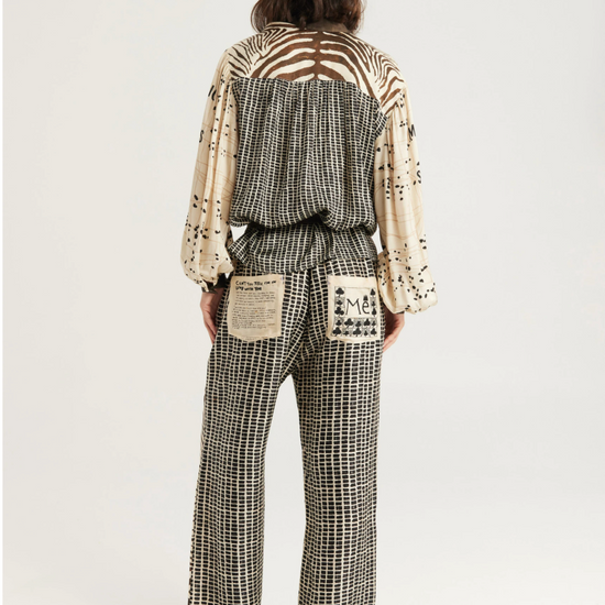 A model shown from the back wearing a two-piece outfit with a black and white houndstooth patterned jumpsuit and a cream-colored long-sleeve top with black abstract patterns and a cutout back.
