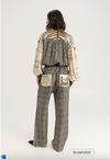 A model shown from the back wearing a two-piece outfit with a black and white houndstooth patterned jumpsuit and a cream-colored long-sleeve top with black abstract patterns and a cutout back.