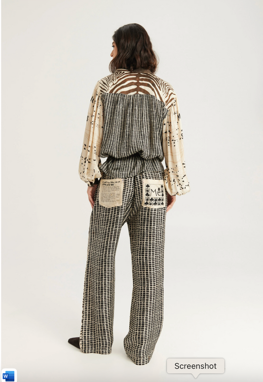 A model shown from the back wearing a two-piece outfit with a black and white houndstooth patterned jumpsuit and a cream-colored long-sleeve top with black abstract patterns and a cutout back.