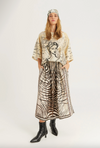 A model stands against a light gray studio background wearing a beige and black graphic print tunic top, a matching long skirt with a zebra-like pattern, a headband, and black pointed ankle boots.