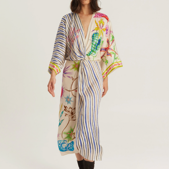 A model wearing a long-sleeved wrap robe with a vertical striped base and colorful botanical and sea-creature prints, paired with black ankle boots, against a plain light gray studio background.