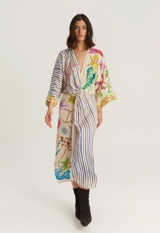 A model wearing a long-sleeved wrap robe with a vertical striped base and colorful botanical and sea-creature prints, paired with black ankle boots, against a plain light gray studio background.