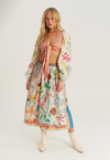 A model wearing a matching two-piece outfit featuring a red and white gingham tie-front crop top and a long-sleeved midi skirt with a colorful botanical print, styled with cream ankle boots against a light gray studio background.