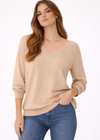 Woman wearing a beige sweater with lace details and blue jeans on a white background
