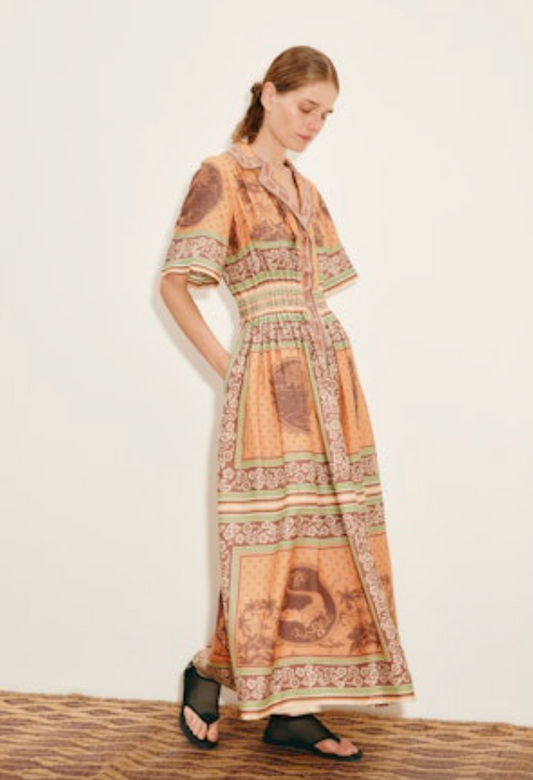 Woman wearing a long, patterned dress against a white wall.