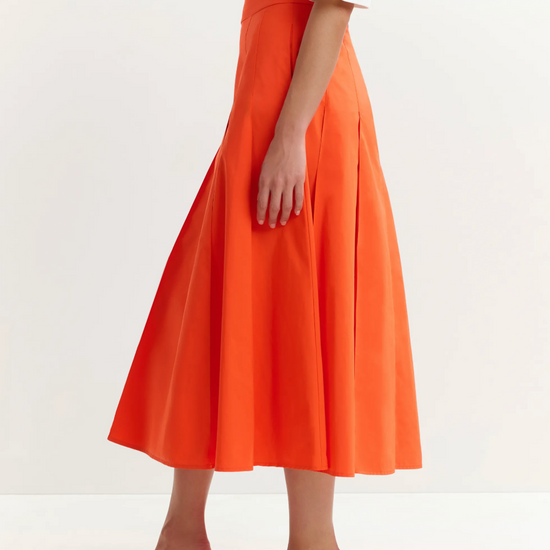 Person wearing an orange skirt with a white top on a white background