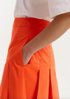 Person wearing an orange skirt with a white top on a light background