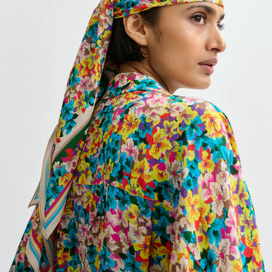 Person wearing a colorful floral headscarf and outfit on a plain background