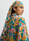 Person wearing a colorful floral headscarf and outfit on a plain background