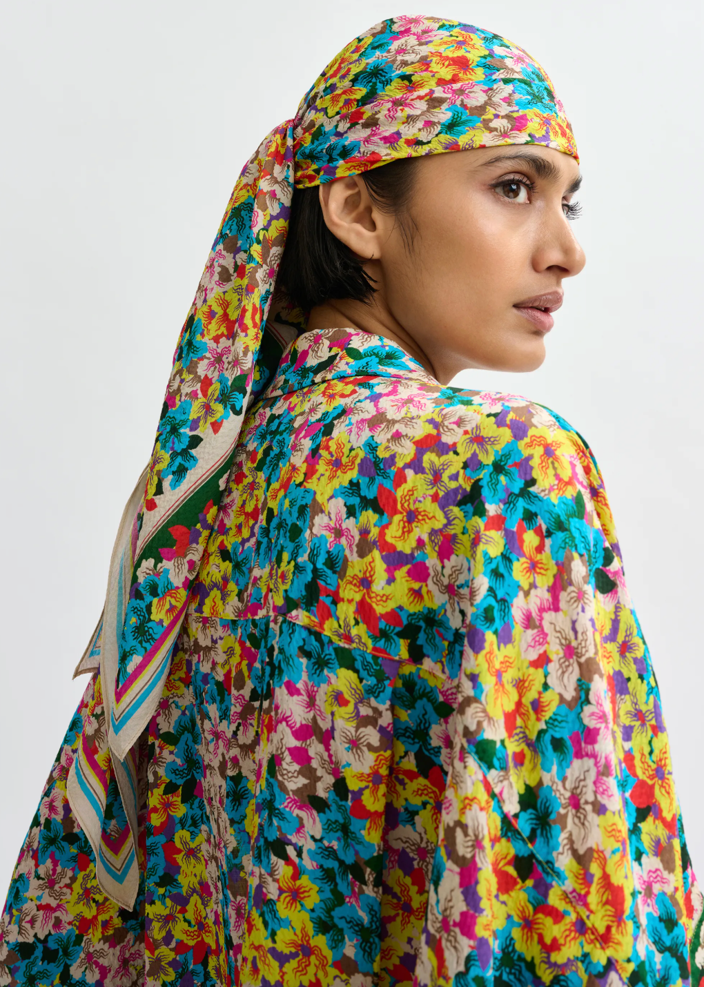 Person wearing a colorful floral headscarf and outfit on a plain background