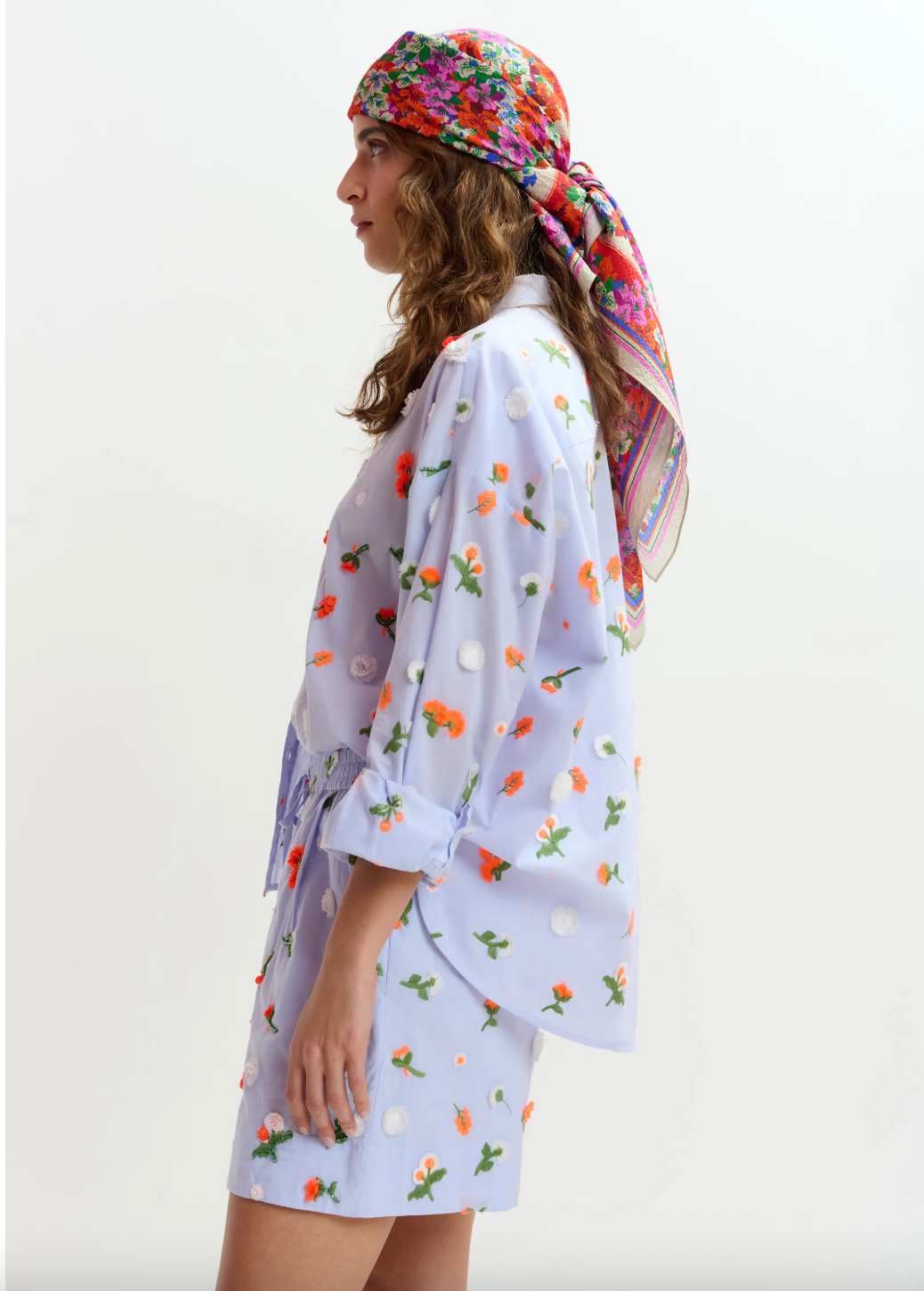 Woman wearing a floral headscarf and a light-colored outfit with floral patterns on a white background