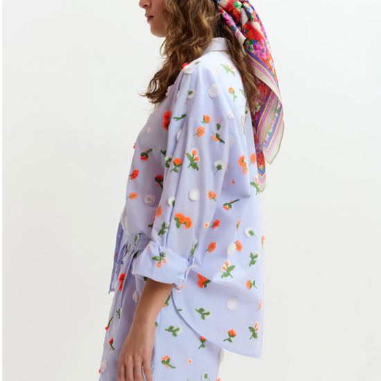 Woman wearing a floral headscarf and a light-colored outfit with floral patterns on a white background