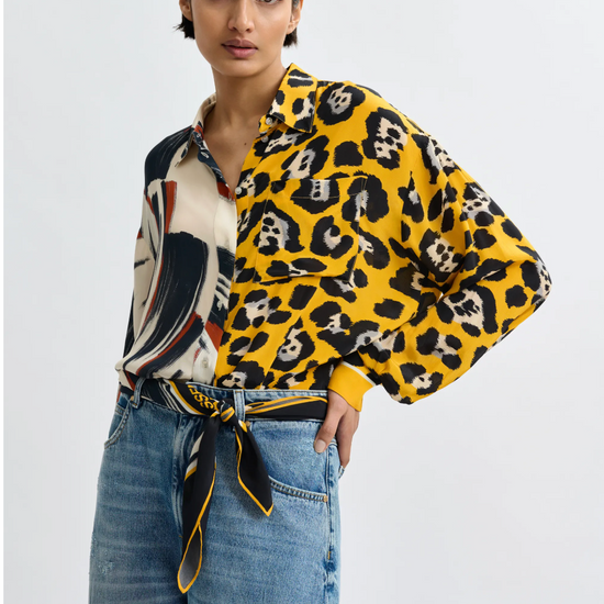 Woman wearing a yellow leopard print shirt with a patterned scarf, standing against a plain background