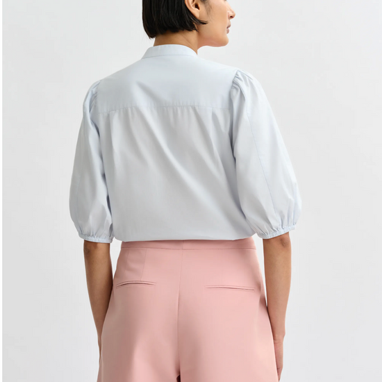 Person wearing a light blue blouse and pink pants on a white background