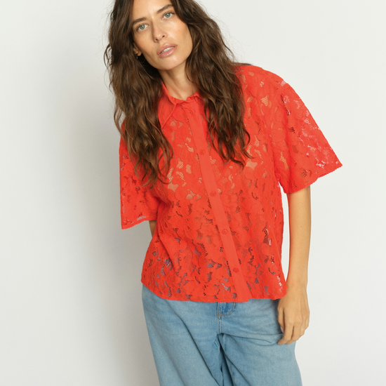 Woman wearing a orange lace top and blue jeans against a white background