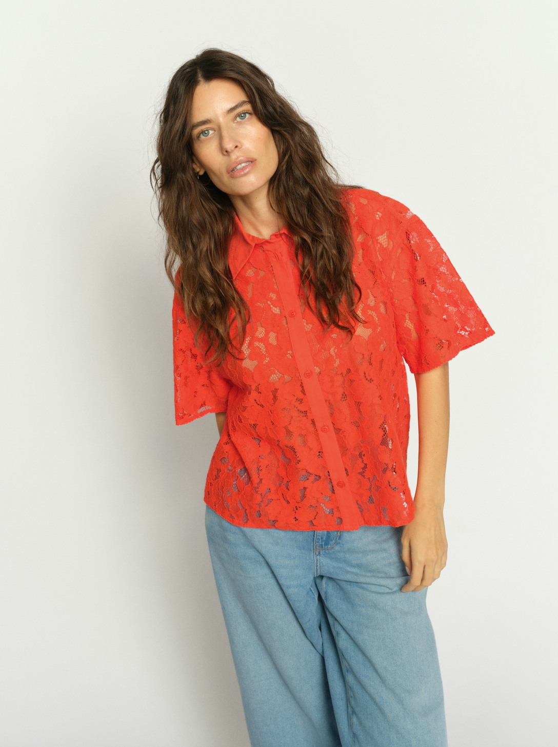 Woman wearing a orange lace top and blue jeans against a white background