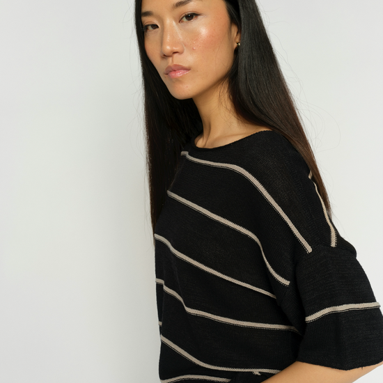 Woman wearing a black sweater with white stripes against a plain background