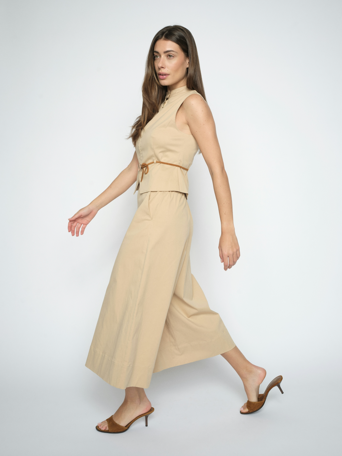 Woman wearing a beige sleeveless top and wide-leg pants on a white background