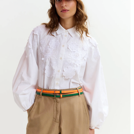 Person wearing a white shirt, beige pants, and an orange cap on a plain background from Essentiel Antwerp
